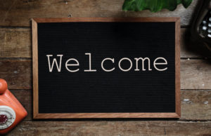 A black sign on a wooden counter says WELCOME in white letters, surrounded by 2 old-fashioned phones and a green leaf