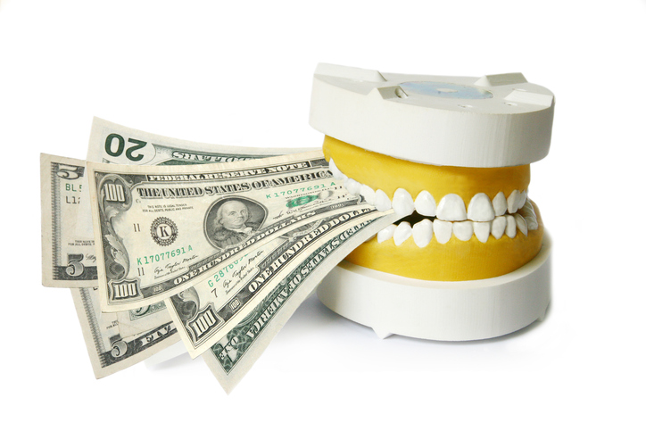 Dental implant cost - Fake teeth biting down on money on a white background