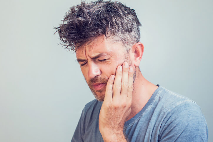 Man in blue shirt holding his mouth in pain