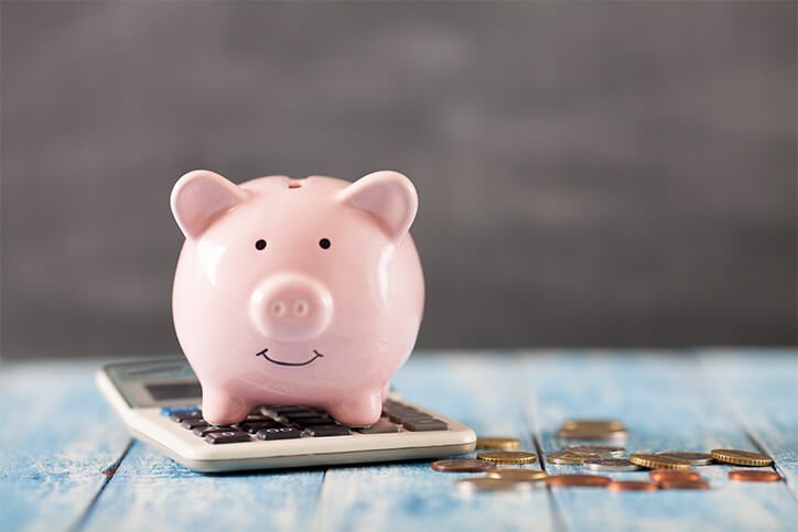 pink piggy bank on top of a calculator with coins all around