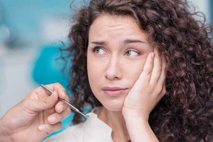 A woman with brown curly hair holding the side of her cheek from tooth pain