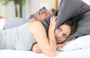 woman covering her ears with a pillow to block out her partners snoring from sleep apnea